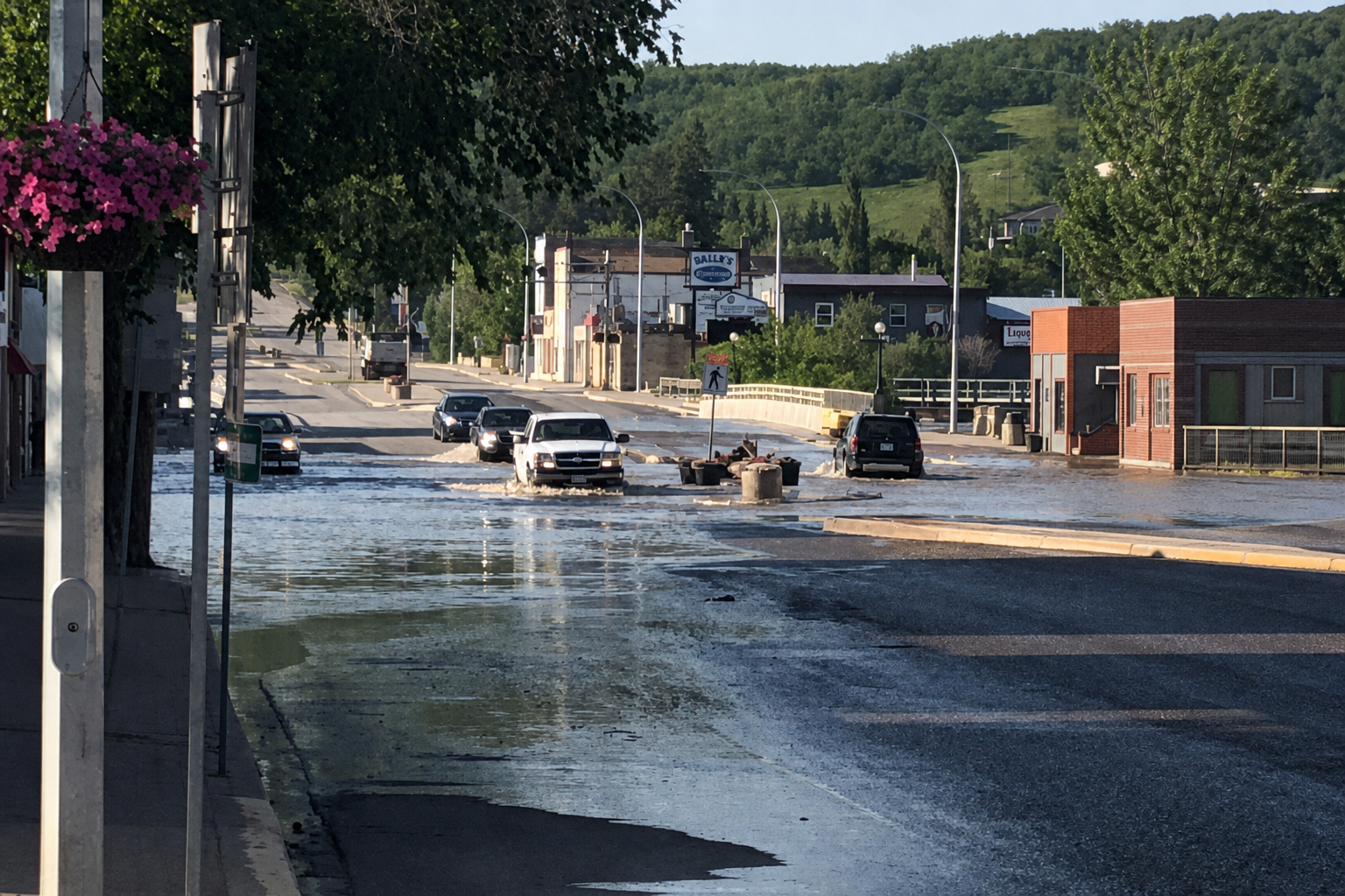 Floodwater covering Main Street in downtown Minnedosa as vehicles drive through